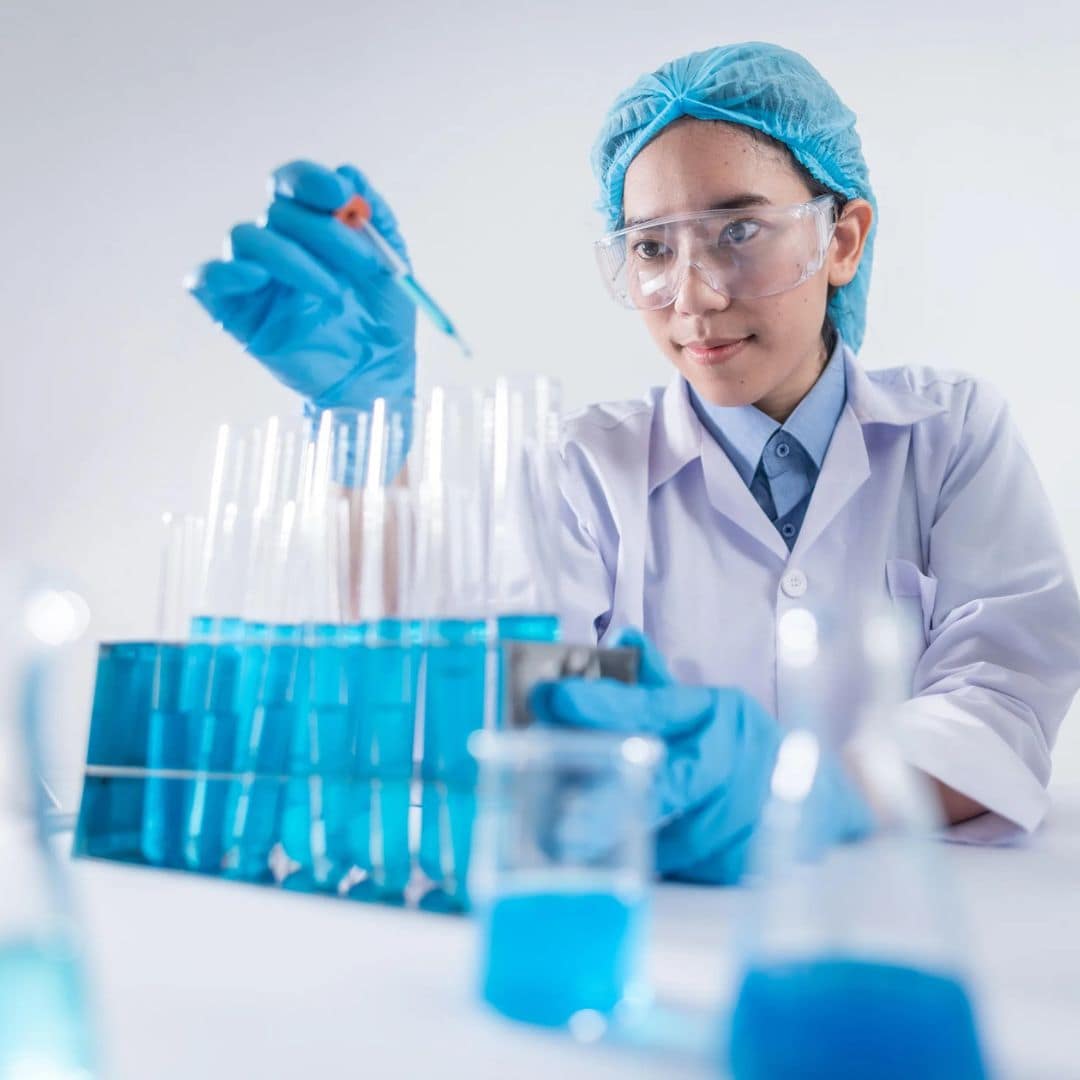 Pharmacologists A scientist pursuing chemistry careers wears protective gear and uses a pipette with test tubes of blue liquid in a laboratory, surrounded by a microscope and glassware.
